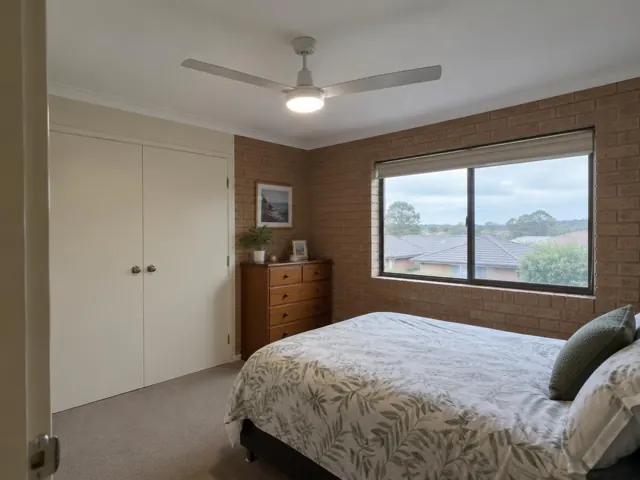 Ceiling fan in a carpeted bedroom with brick walls, a window and built-in wardrobe in Speers Point