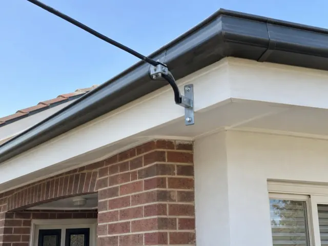 Overhead service cable with bracket on a brick and rendered house exterior in Argenton