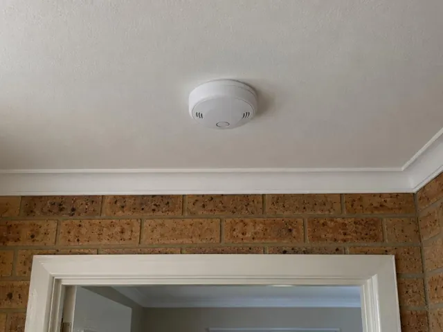 Ceiling-mounted smoke alarm above a doorway in a brick interior in Speers Point